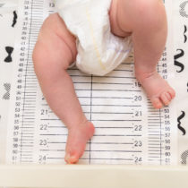 Cropped shot of a pediatrician examining newborn baby. Doctor using measurement tape checking baby's size. Closeup